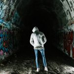 man in gray hoodie walking on tunnel
