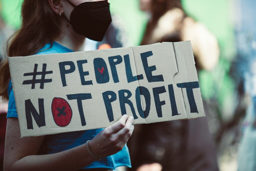 a woman holding a sign that says people not profits